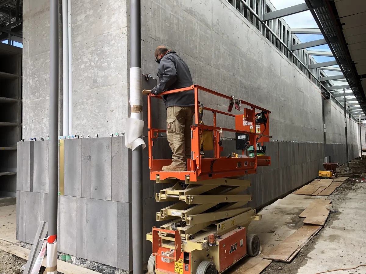 Installer securing large format stone cladding panel on a facade using a scissor lift