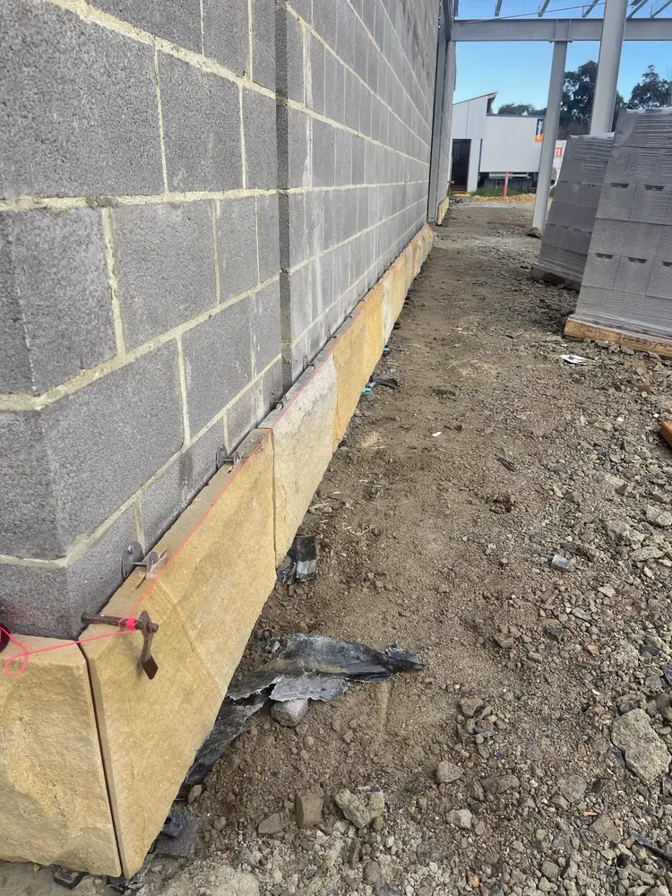 Mechanical fixing brackets and pins anchoring sandstone base cladding to a block wall