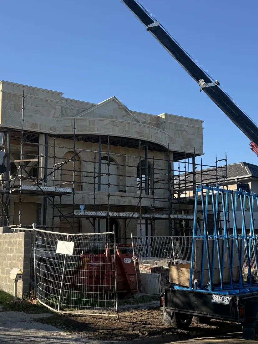 Exterior sandstone cladding installation underway with crane support