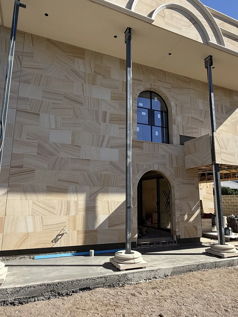 Completed sandstone façade section with an arched window and columns