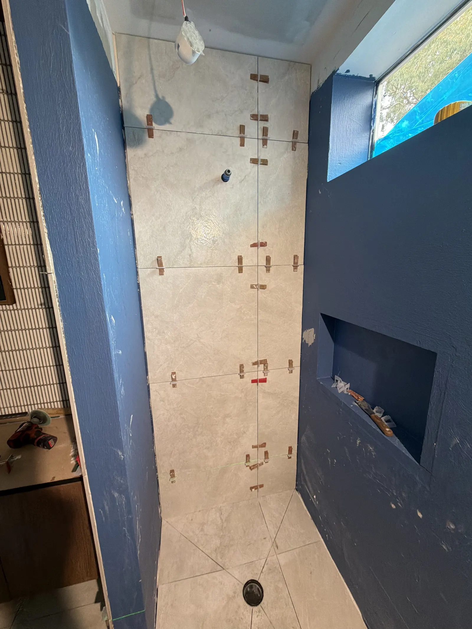 Large-format porcelain tile being installed on bathroom wall