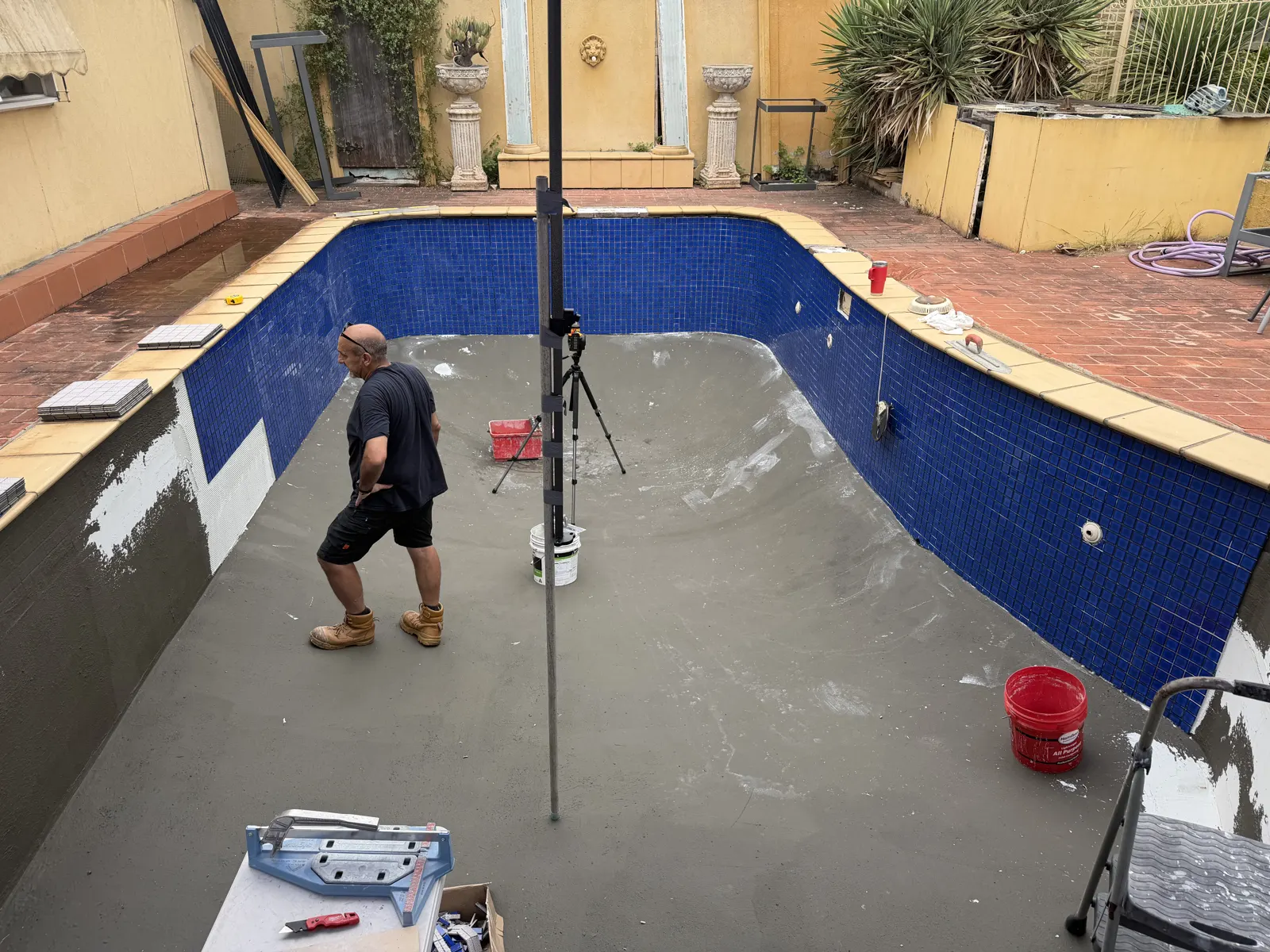 Pool walls fully tiled in dark blue glass mosaic, floor still bare