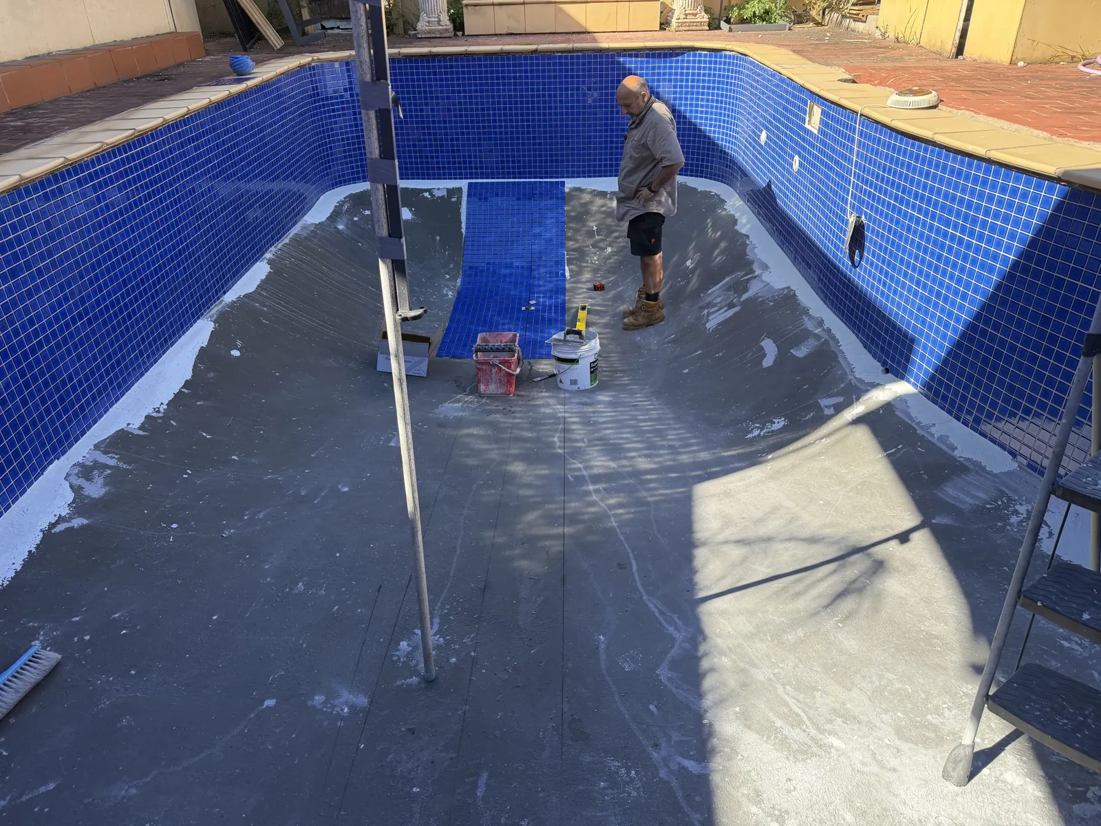 Tiling the pool floor in dark blue glass mosaic over waterproofed substrate
